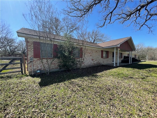 view of side of home with a yard, brick siding, a patio, and fence