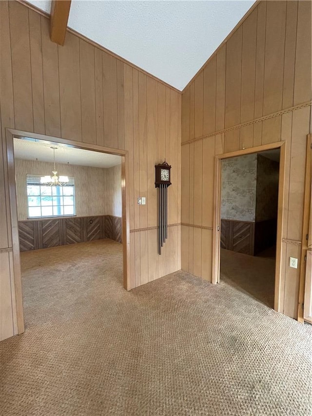 unfurnished room featuring a chandelier, carpet, lofted ceiling, and wooden walls