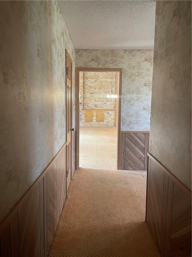 hallway featuring a textured ceiling, carpet floors, wainscoting, and wallpapered walls