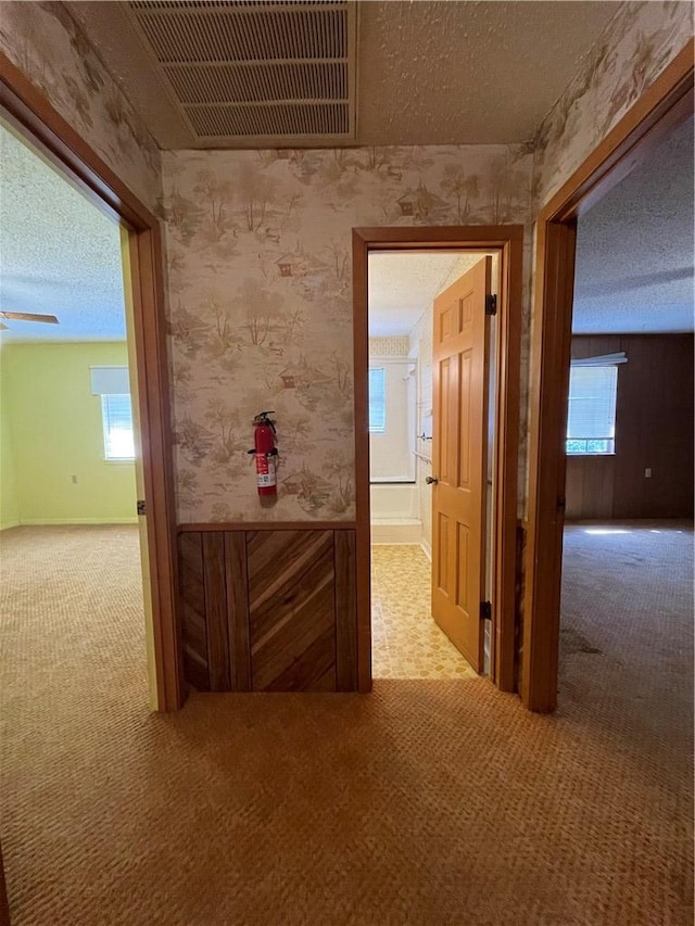 hall featuring a textured ceiling, visible vents, and carpet flooring