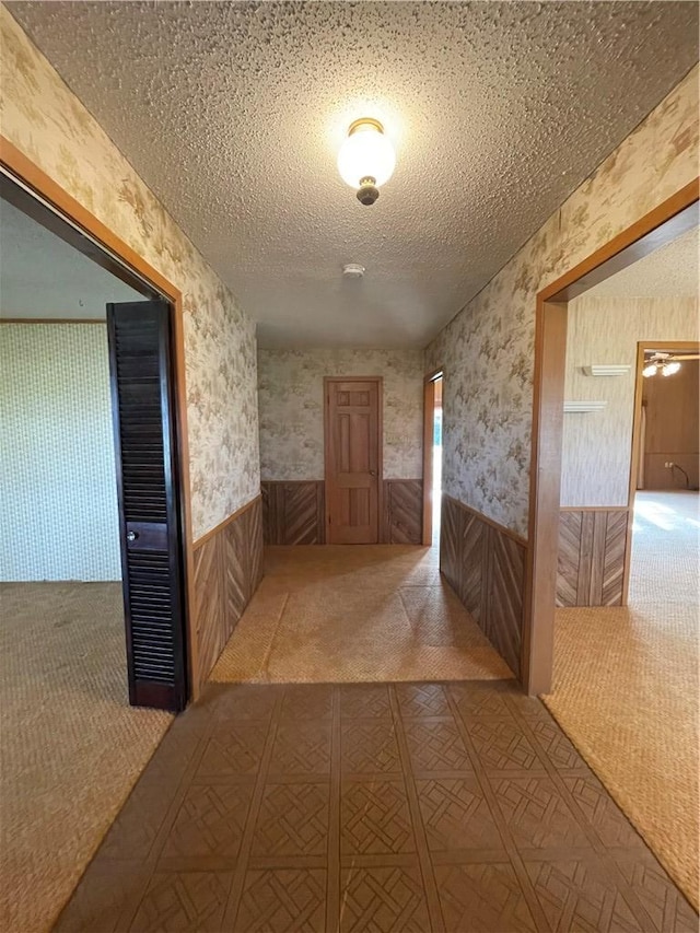 corridor featuring carpet, wainscoting, a textured ceiling, and wallpapered walls