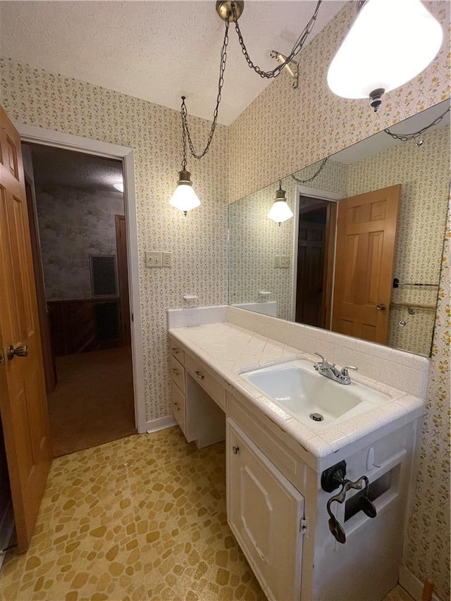 bathroom featuring a textured ceiling, stone finish flooring, vanity, and wallpapered walls