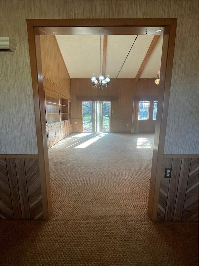 carpeted spare room featuring an inviting chandelier, high vaulted ceiling, and wood walls