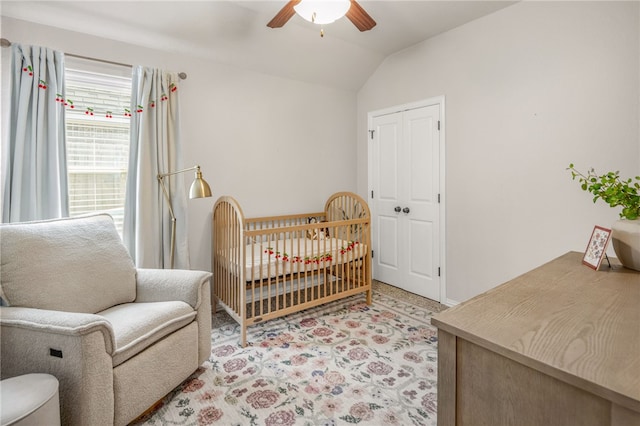 bedroom with lofted ceiling, light carpet, a ceiling fan, a closet, and a nursery area