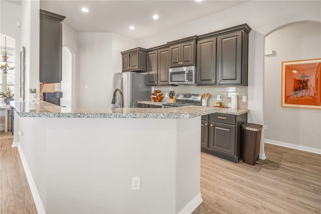 kitchen with arched walkways, recessed lighting, stainless steel appliances, light wood-type flooring, and light stone countertops