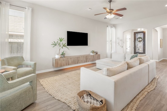 living area with arched walkways, a ceiling fan, a wealth of natural light, and light wood-style floors