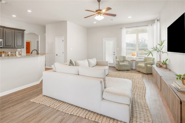 living area with arched walkways, recessed lighting, visible vents, light wood-style floors, and a ceiling fan