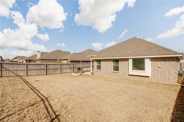 rear view of house with a fenced backyard, a shingled roof, and brick siding