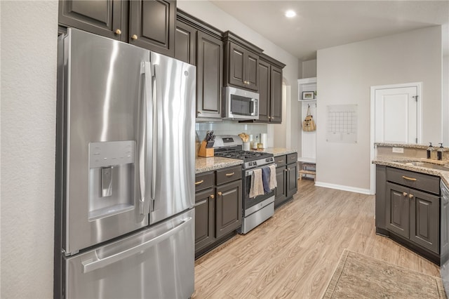 kitchen featuring stainless steel appliances, decorative backsplash, light wood-style floors, dark brown cabinets, and light stone countertops