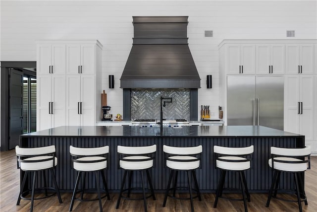 1923 County Road 202, Caldwell, TX 77836 - kitchen featuring built in fridge, custom range hood, wood finished floors, decorative backsplash, and white cabinetry