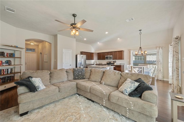 living room with ceiling fan with notable chandelier, light hardwood / wood-style floors, vaulted ceiling, and sink