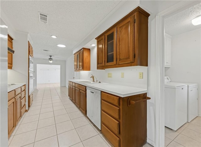 kitchen with sink, stainless steel dishwasher, independent washer and dryer, light tile patterned floors, and a textured ceiling