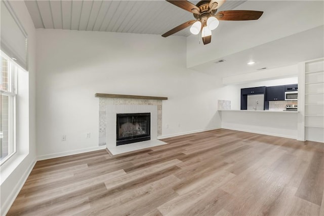 unfurnished living room featuring a tiled fireplace, ceiling fan, and wood-type flooring