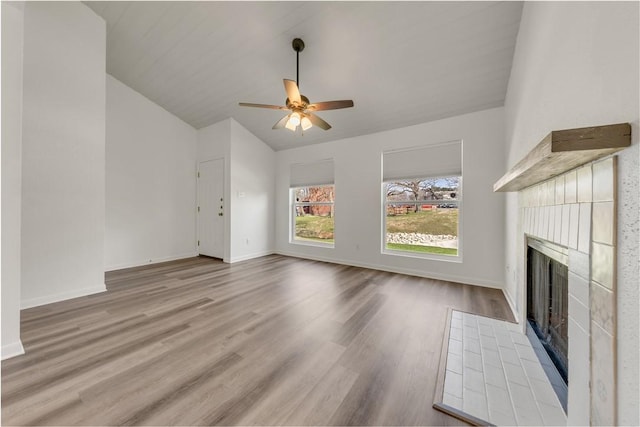 unfurnished living room with ceiling fan, a tile fireplace, vaulted ceiling, and light hardwood / wood-style floors