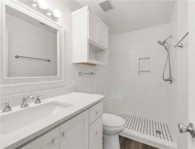 bathroom with hardwood / wood-style flooring, toilet, vanity, and tiled shower