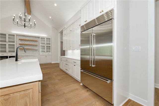 kitchen with white cabinets, stainless steel built in fridge, and vaulted ceiling