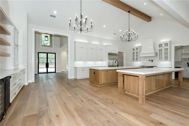 kitchen with white cabinetry, light hardwood / wood-style flooring, beamed ceiling, a large island with sink, and custom exhaust hood