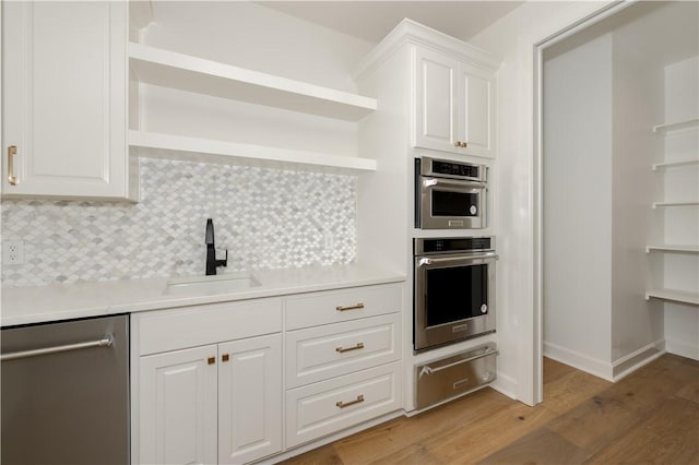 kitchen featuring sink, backsplash, wood-type flooring, white cabinets, and appliances with stainless steel finishes