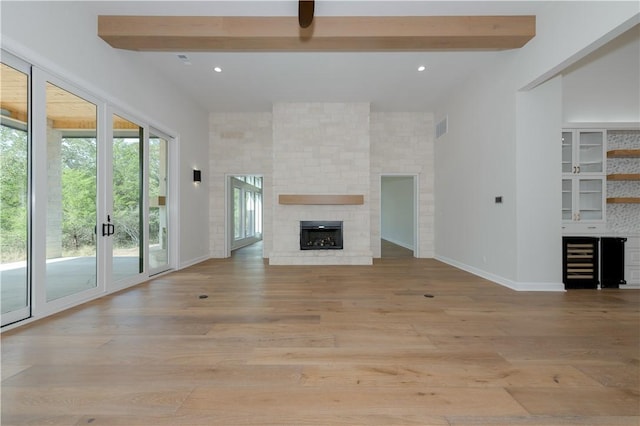 unfurnished living room with beam ceiling, french doors, beverage cooler, light hardwood / wood-style floors, and a fireplace