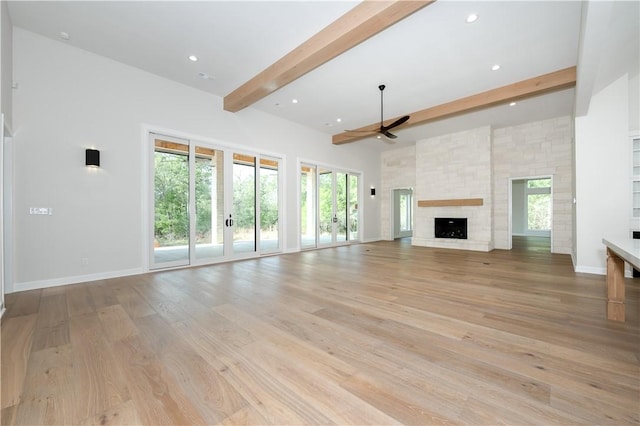 unfurnished living room with plenty of natural light, beam ceiling, a stone fireplace, and light hardwood / wood-style flooring