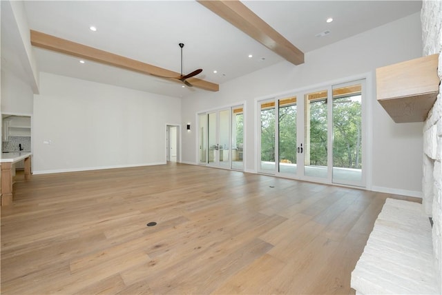 unfurnished living room with beam ceiling, ceiling fan, french doors, a stone fireplace, and light hardwood / wood-style flooring