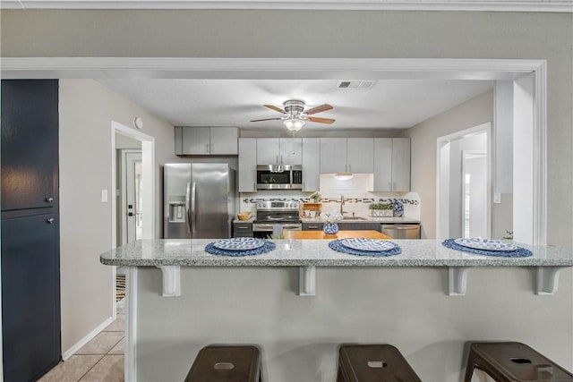 kitchen featuring gray cabinets, a breakfast bar area, and appliances with stainless steel finishes