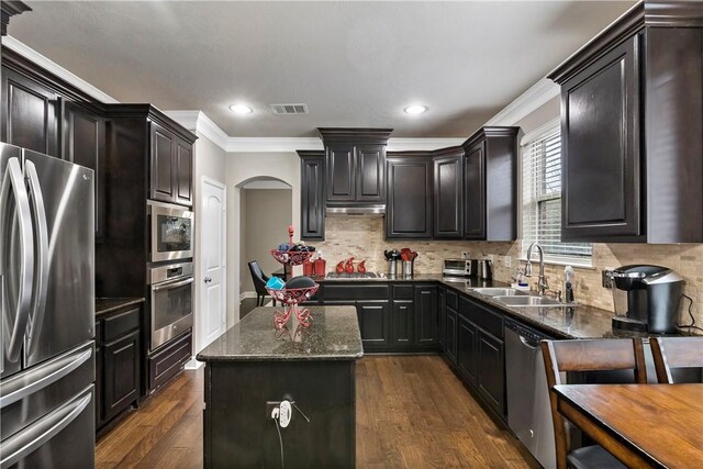 kitchen with ornamental molding, stainless steel appliances, dark wood-type flooring, sink, and a center island