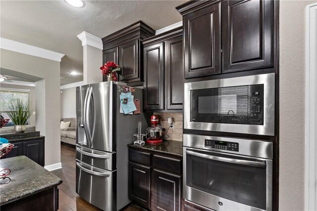 kitchen with dark stone counters, ornamental molding, appliances with stainless steel finishes, dark hardwood / wood-style flooring, and dark brown cabinetry