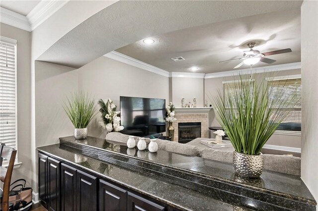 interior space with ceiling fan, ornamental molding, a textured ceiling, and a tiled fireplace