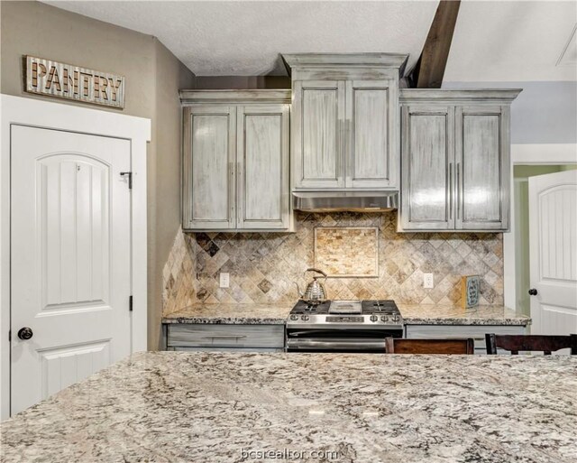 kitchen with beam ceiling, light stone counters, tasteful backsplash, and gas range