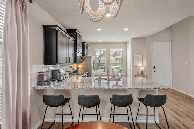 808 Mineral Wells Ln, College Station, TX 77845 - kitchen featuring a peninsula, appliances with stainless steel finishes, light wood-type flooring, light stone counters, and recessed lighting