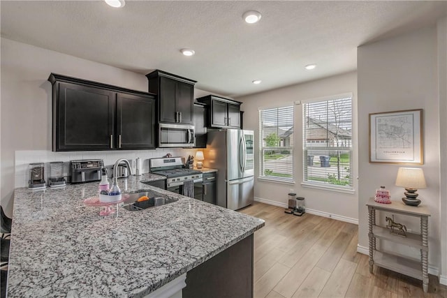 808 Mineral Wells Ln, College Station, TX 77845 - kitchen featuring appliances with stainless steel finishes, light stone counters, backsplash, light wood-style flooring, and dark cabinets