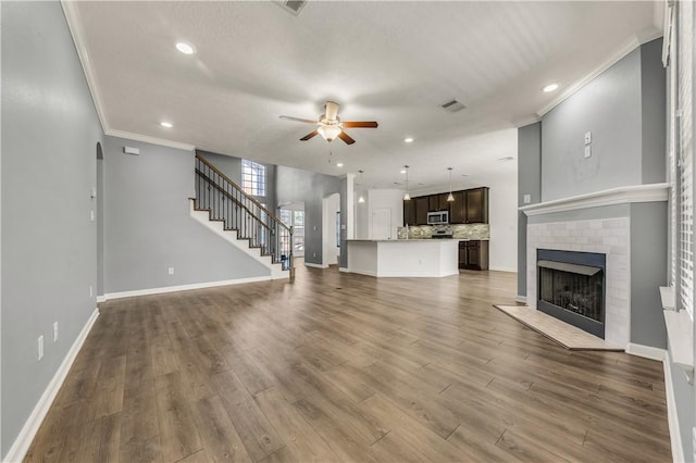 unfurnished living room featuring hardwood / wood-style flooring, ceiling fan, ornamental molding, and a fireplace