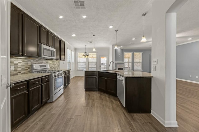 kitchen with appliances with stainless steel finishes, decorative light fixtures, sink, decorative backsplash, and light stone counters