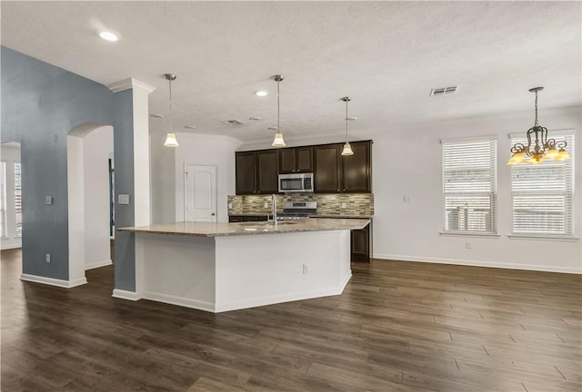 kitchen featuring sink, stainless steel appliances, dark brown cabinetry, light stone countertops, and an island with sink