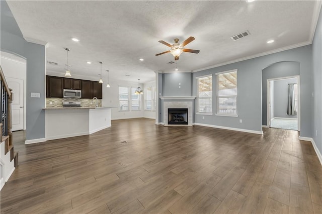 unfurnished living room featuring a tiled fireplace, ornamental molding, ceiling fan, and dark hardwood / wood-style flooring