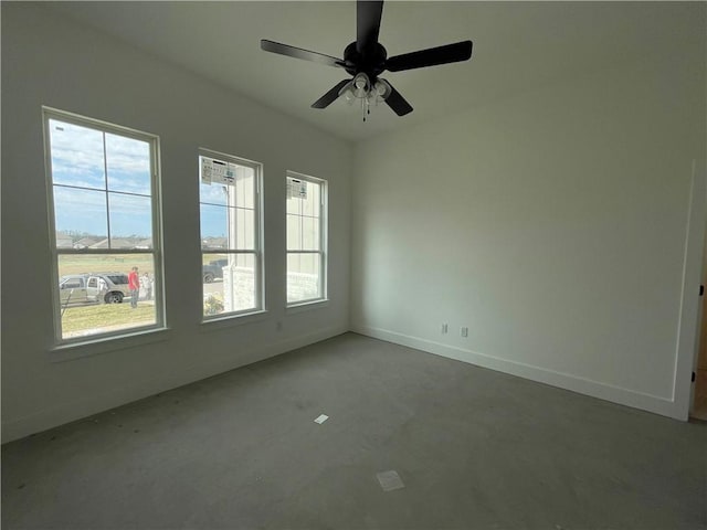 spare room with plenty of natural light, concrete floors, baseboards, and ceiling fan