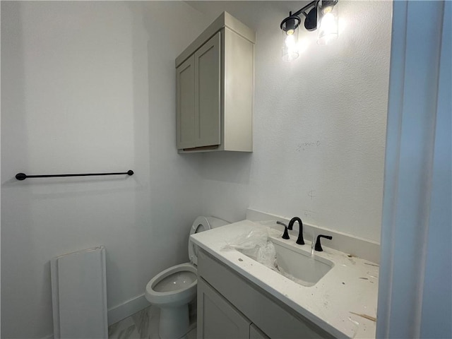 half bath with toilet, marble finish floor, baseboards, and vanity