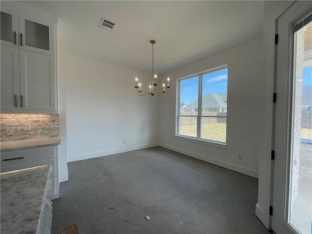 unfurnished dining area with visible vents, unfinished concrete flooring, baseboards, and an inviting chandelier