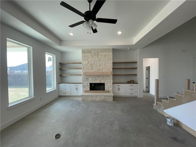 unfurnished living room featuring baseboards, unfinished concrete flooring, a tray ceiling, a fireplace, and recessed lighting