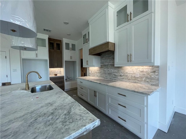 kitchen featuring visible vents, glass insert cabinets, light stone countertops, white cabinetry, and a sink