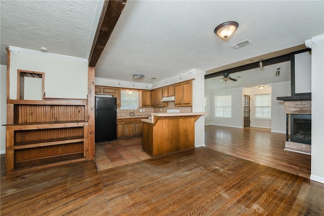 kitchen featuring backsplash, black refrigerator, dark hardwood / wood-style floors, ceiling fan, and a textured ceiling