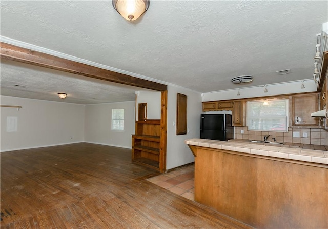 kitchen with black refrigerator, tasteful backsplash, a textured ceiling, tile countertops, and light hardwood / wood-style flooring