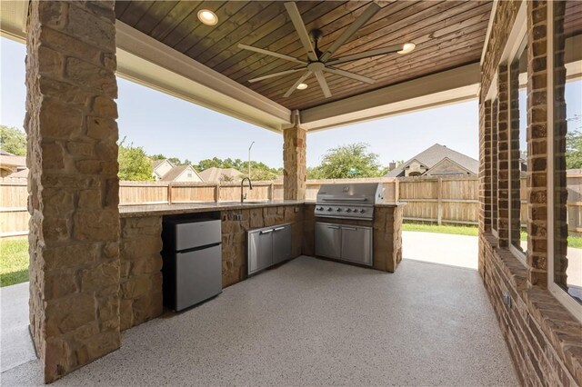 view of patio featuring exterior kitchen, area for grilling, ceiling fan, fence, and a sink