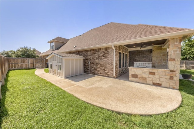 back of house featuring an outdoor kitchen, a ceiling fan, roof with shingles, a patio, and brick siding