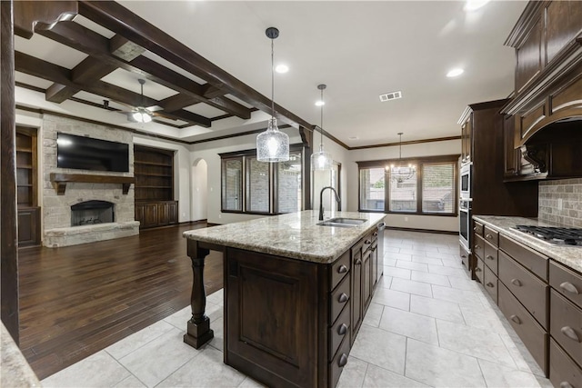 kitchen featuring a sink, appliances with stainless steel finishes, a ceiling fan, ornamental molding, and a center island with sink