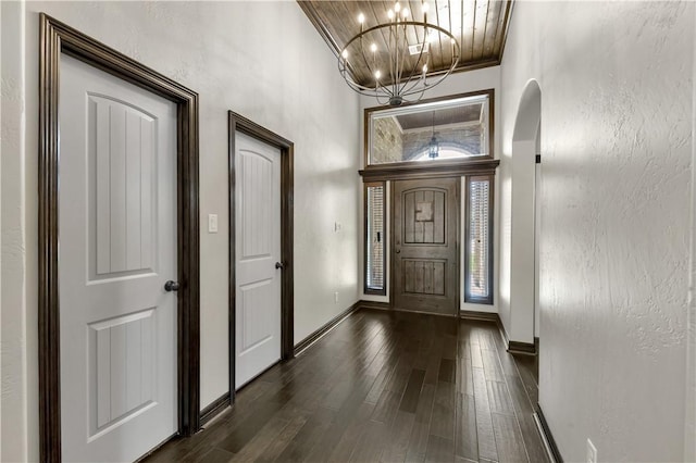 entrance foyer with a chandelier, dark wood-type flooring, baseboards, and arched walkways