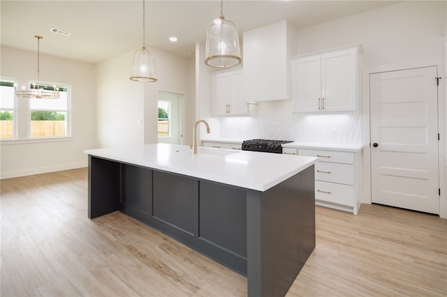 2802 Spector Dr, Bryan, TX 77808 - kitchen featuring decorative backsplash, light wood finished floors, an island with sink, white cabinetry, and gas stove