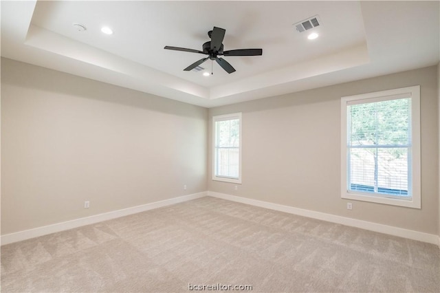 carpeted spare room with a raised ceiling and ceiling fan