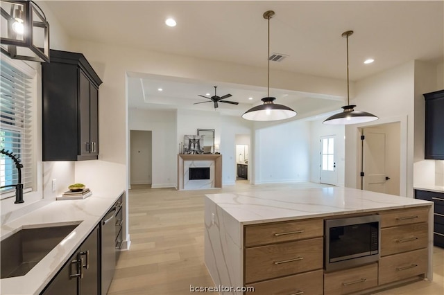 kitchen with ceiling fan, sink, light stone counters, light hardwood / wood-style floors, and appliances with stainless steel finishes